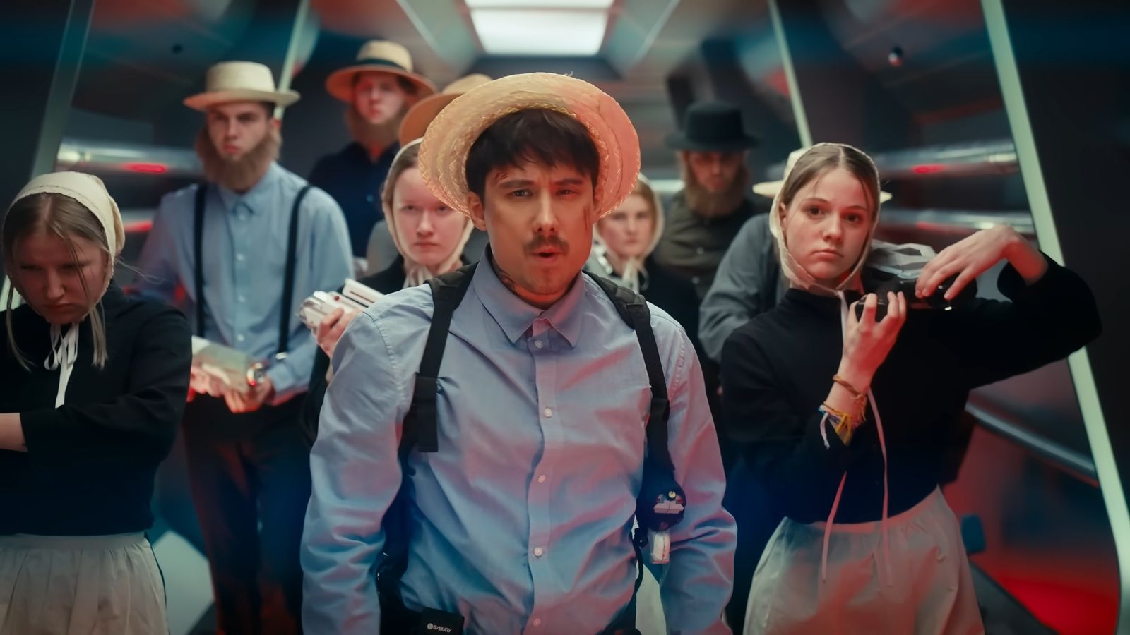 A man in a straw hat leads a group down a spaceship corridor