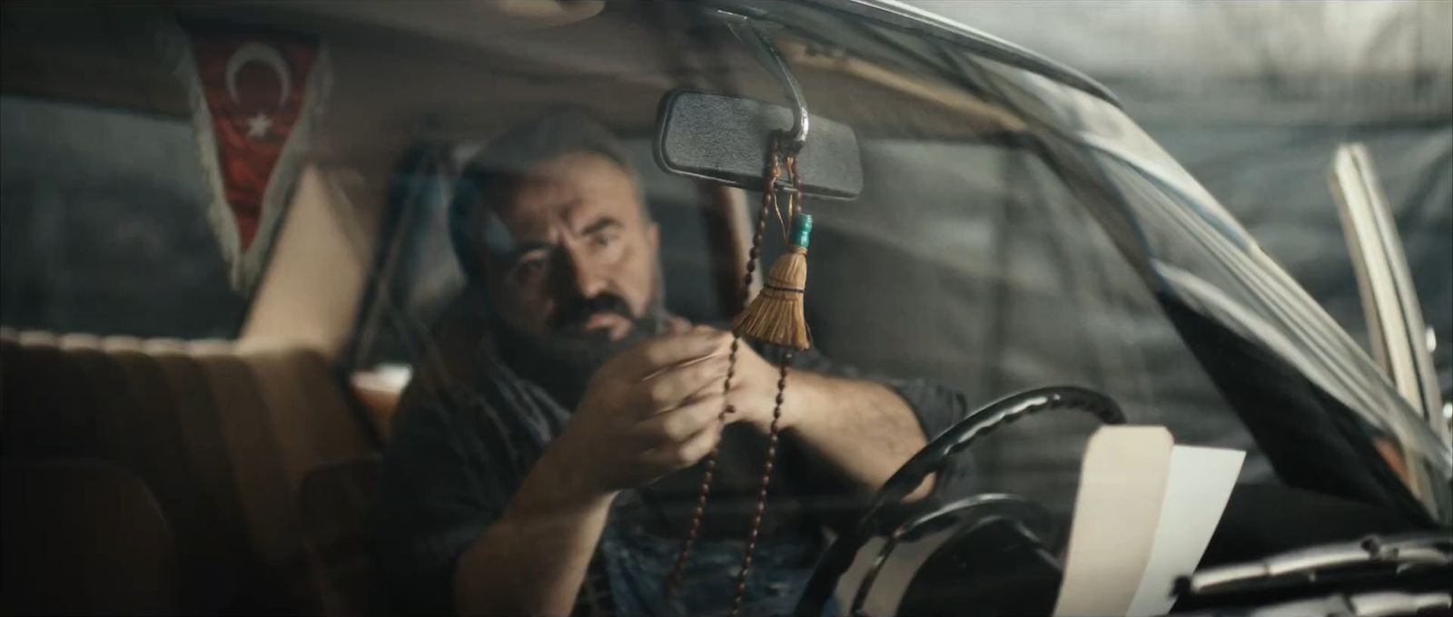 A man behind a windscreen holding prayer beads