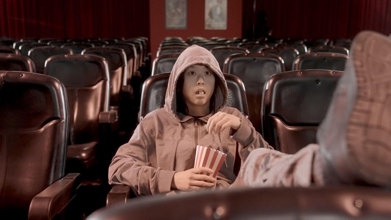 A hooded girl with popcorn in an empty cinema