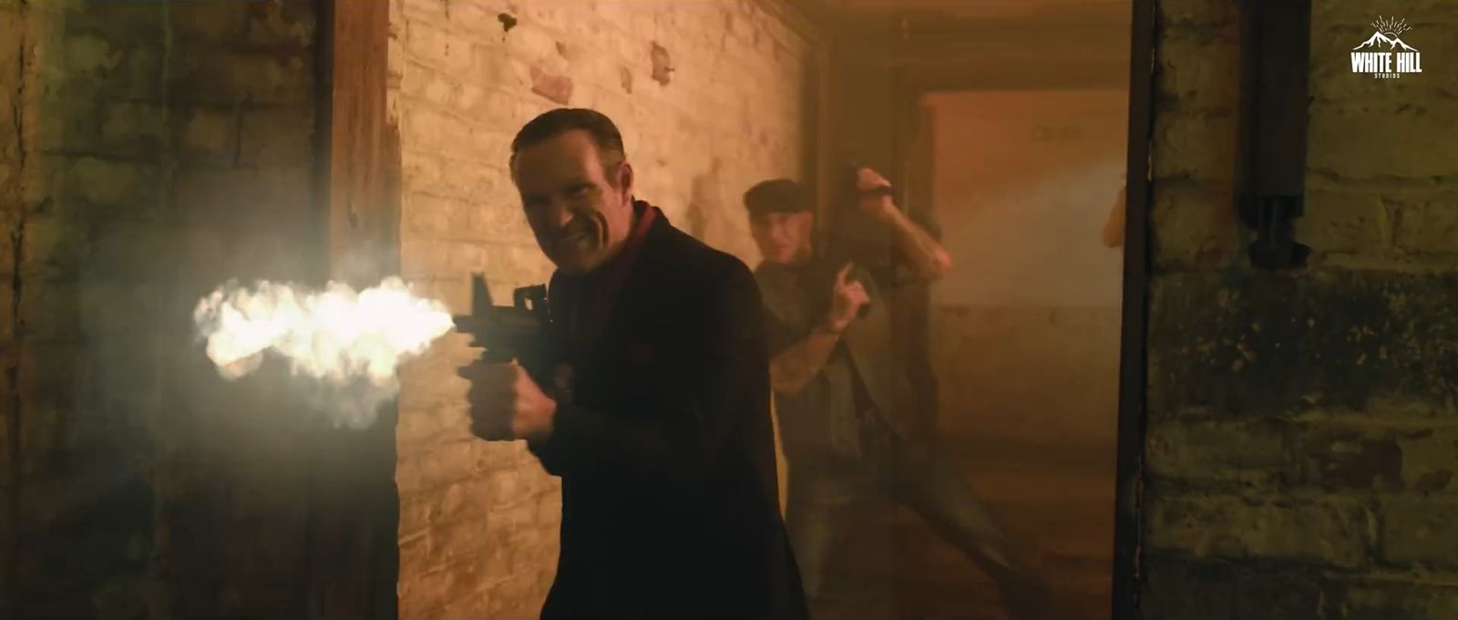 A man fires a gun in a smoky brick corridor