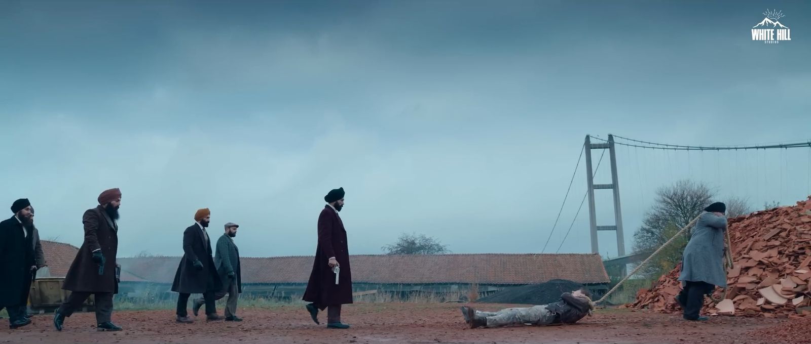 Men in long coats walk across a red quarry