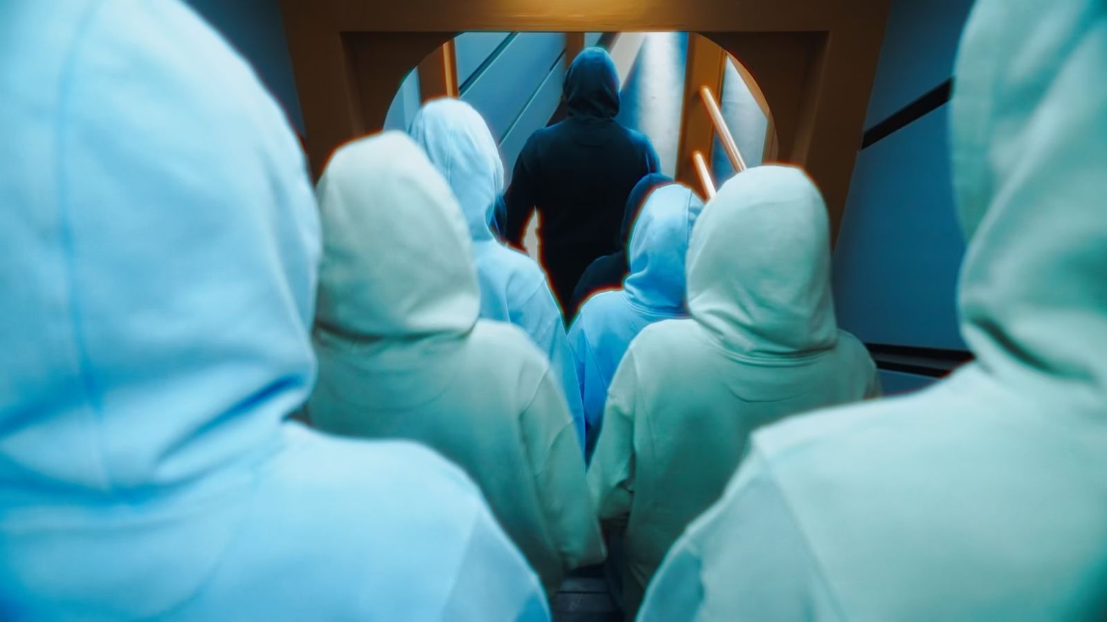Hooded figures follow a dark figure through a round hatch