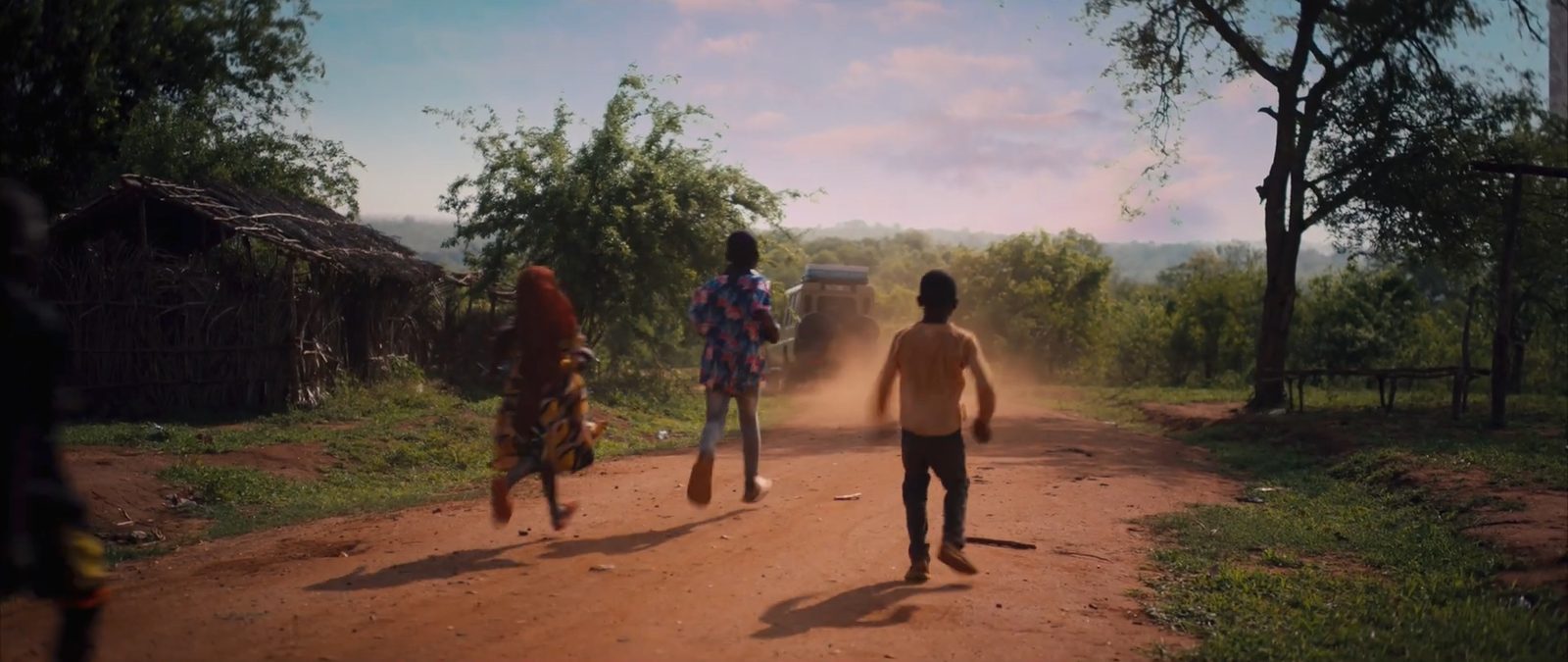 Children run after a jeep down a red dirt road